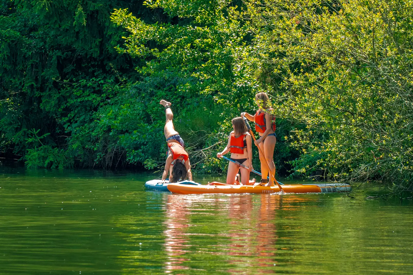 An adult and children on a large paddleboard on the private lake at Domaine du Dahu