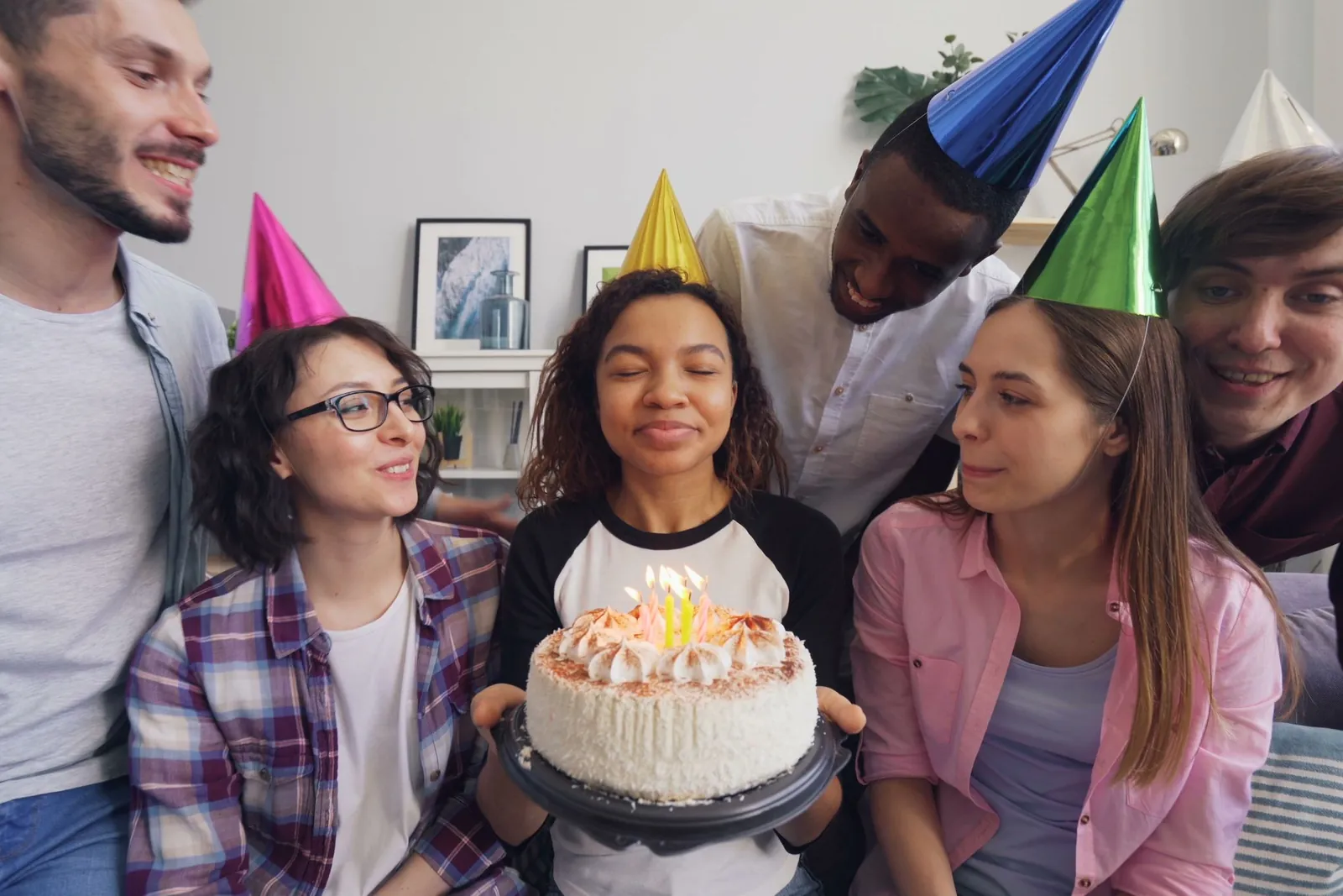 Friends in party hats around a birthday cake with lit candles