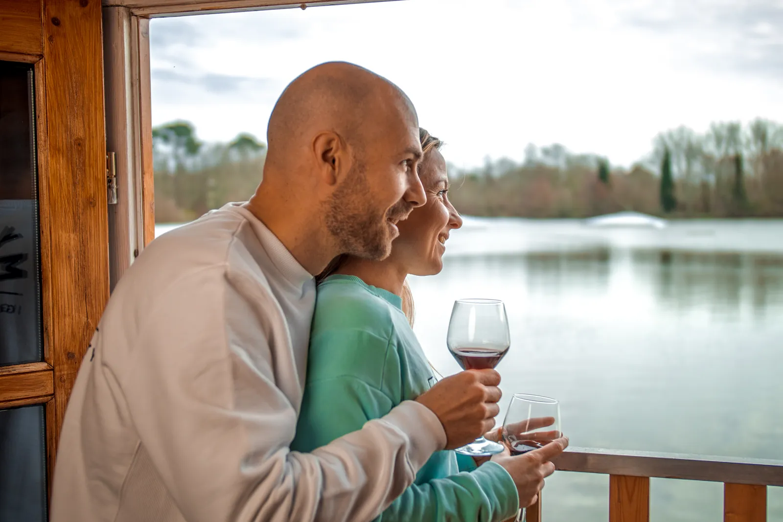Couple embracing with glasses of wine on a floating chalet terrace overlooking the lake