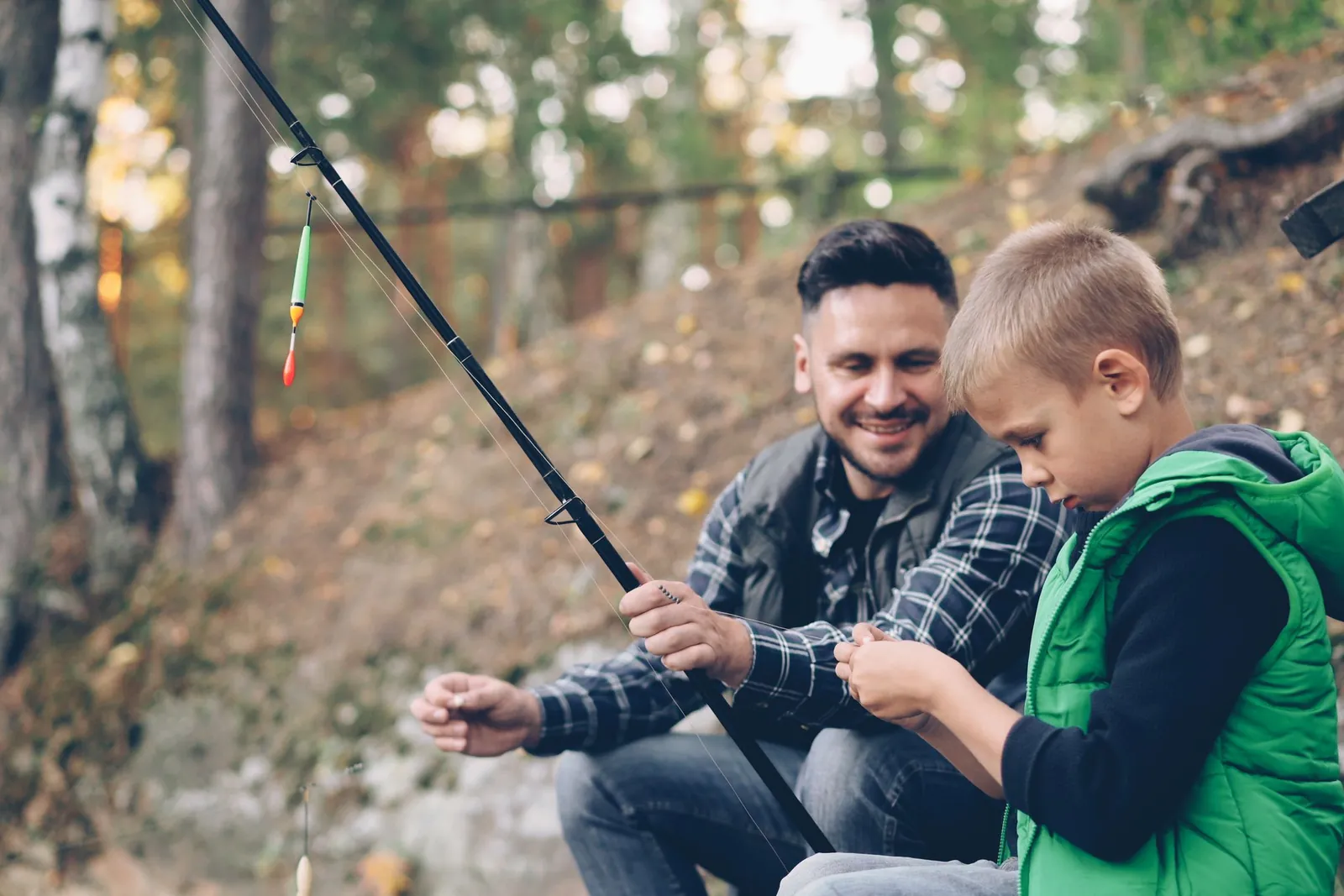 A father and son getting their fishing line ready by the water