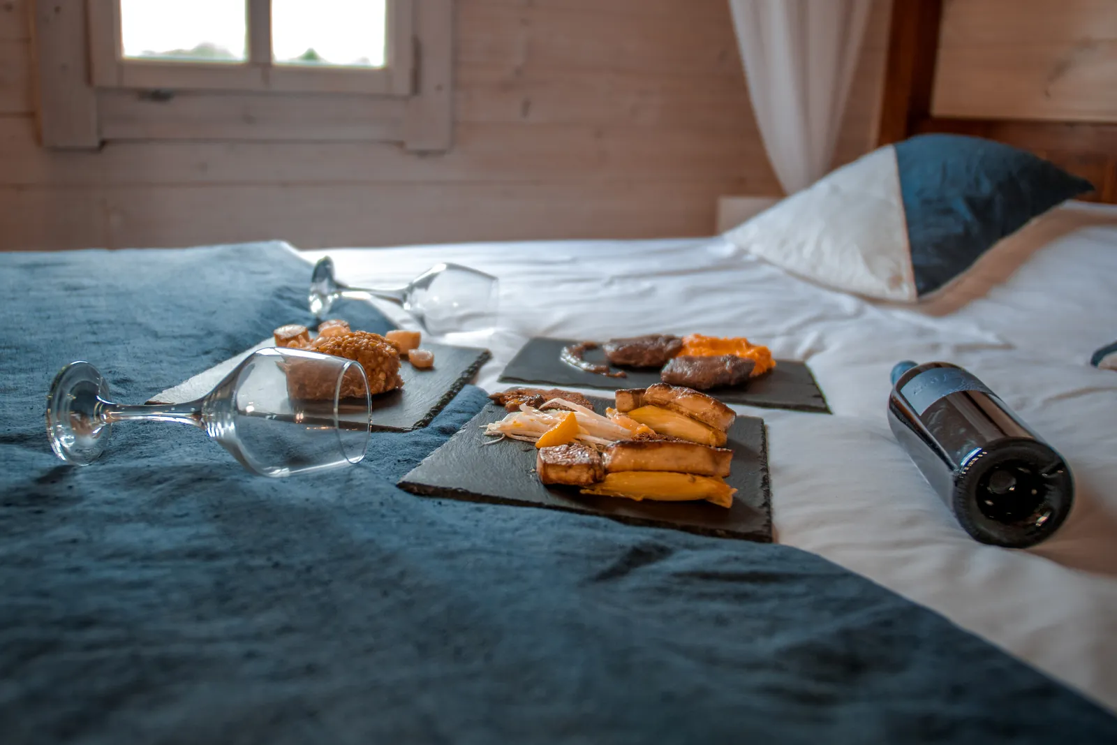 Planches apéritives, verres et bouteille de vin posés sur le lit d'un chalet flottant