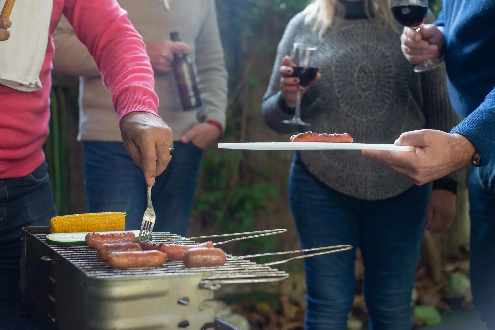 Outdoor barbecue with friends, sausages on the grill and glasses of wine