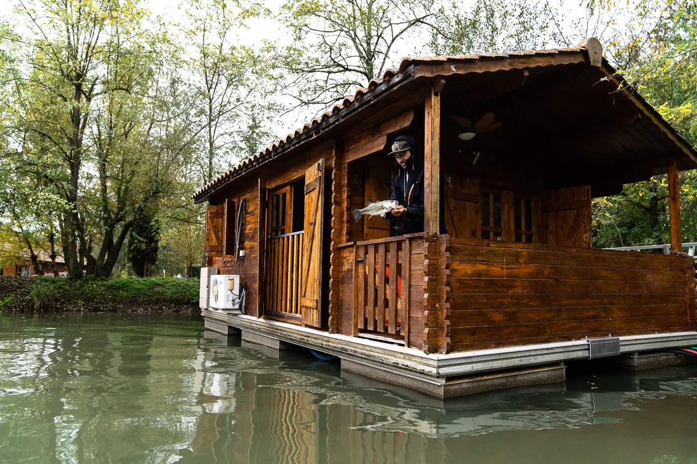 Angler on the terrace of a floating chalet at Domaine du Dahu, holding a fish